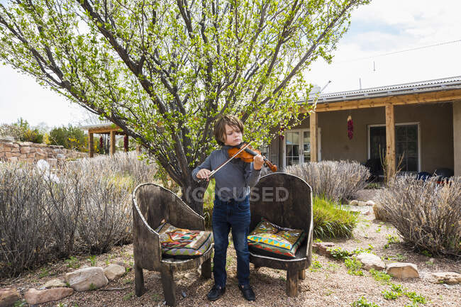 Шестилетний мальчик играет на скрипке возле своего дома — стоковое фото