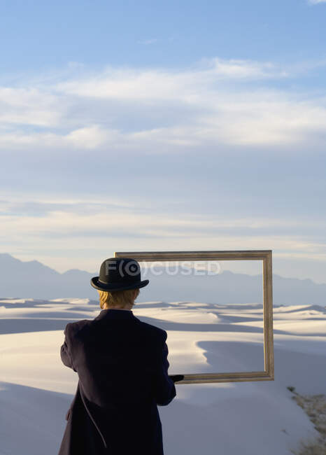 Man in a black coat and suit, a bowler hat and umbrella, in a white desert wilderness of white sand. — Stock Photo