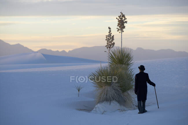 Uomo in giacca e cravatta nera, cappello a bombetta e ombrello, in un deserto bianco di sabbia bianca. — Foto stock