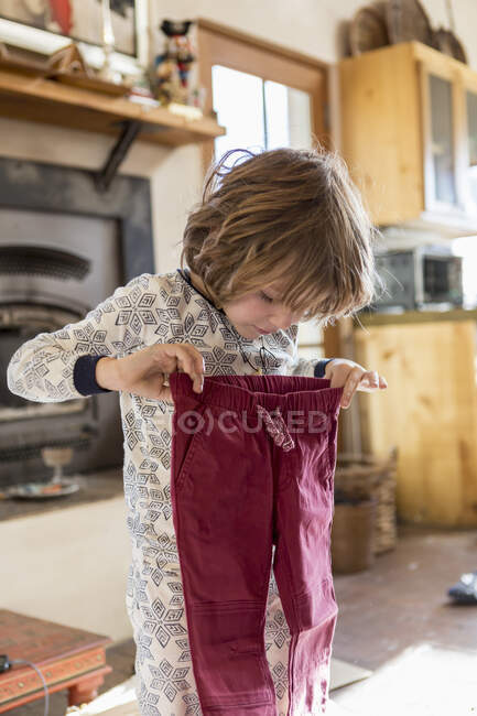 4 anos de idade menino vestindo pijama e segurando calças em casa — Fotografia de Stock