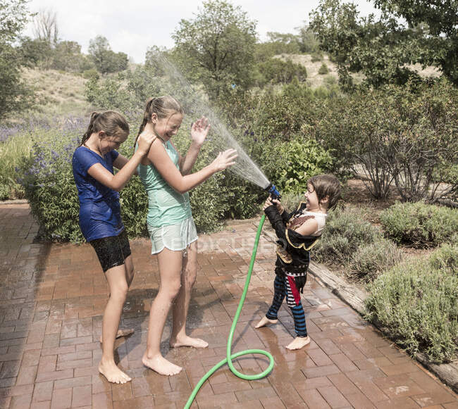 Enfants se vaporisant mutuellement avec un tuyau d'eau — Photo de stock