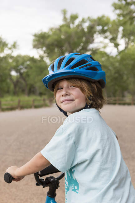 Sorrindo menino de 4 anos de idade em um capacete ciclo olhando por cima de seu ombro. — Fotografia de Stock