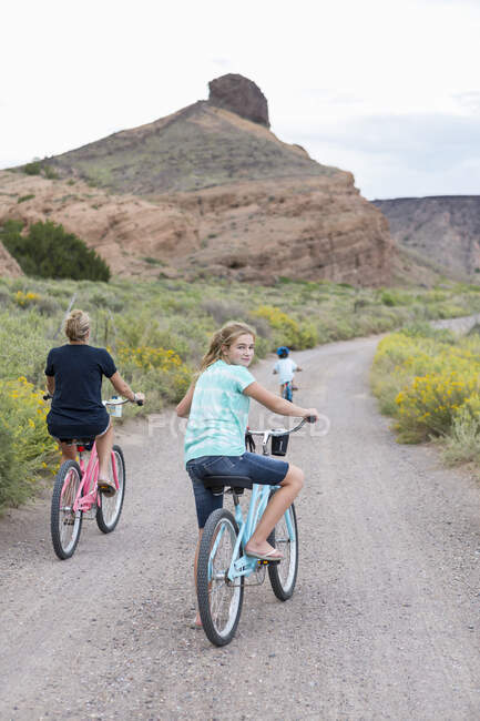 11 años de edad, niña en bicicleta mirando hacia atrás a la cámara mientras monta bicicletas con la familia - foto de stock