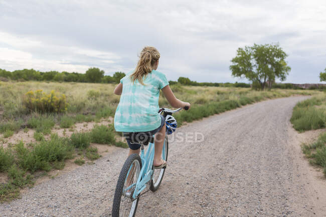 Вид сзади на 11-летнюю девушку, катающуюся на велосипеде по проселочной дороге — стоковое фото