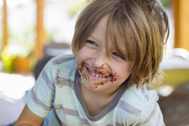Портрет улыбающегося 4-летнего мальчика с шоколадом на лице, играющего и смеющегося — стоковое фото