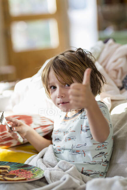 4 ans garçon manger des crêpes sur le canapé — Photo de stock