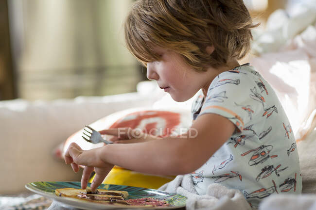 4 year old boy eating pancakes on the sofa — Stock Photo