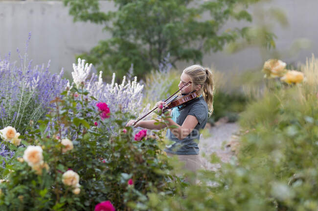 Teenagermädchen steht zwischen blühenden Rosen und Sträuchern und spielt Geige — Stockfoto