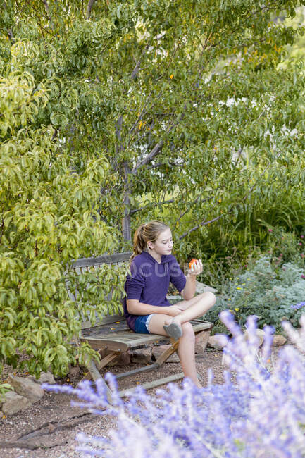 Niña de 11 años sentada en el banco, leyendo un libro - foto de stock