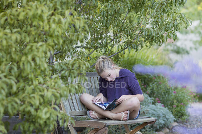 11-jähriges Mädchen sitzt auf Bank und liest ein Buch — Stockfoto