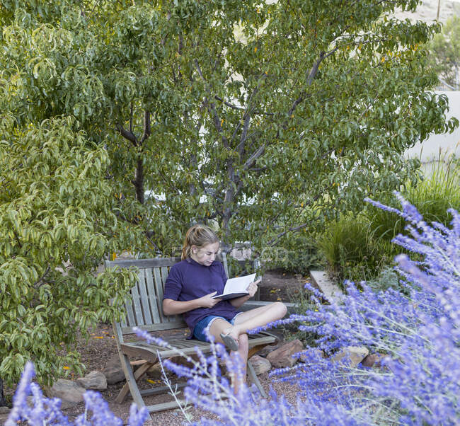 Fille de 11 ans assise sur un banc, lisant un livre — Photo de stock