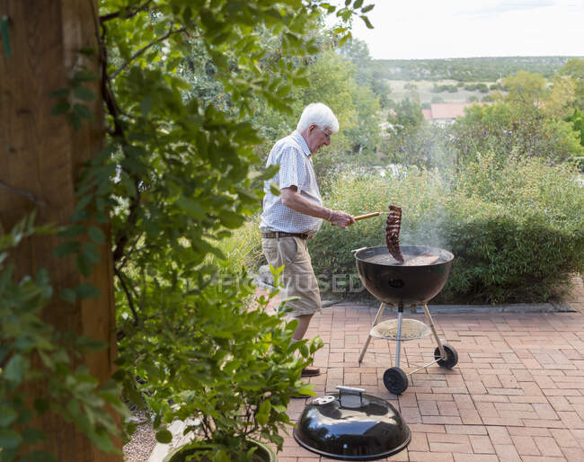 Senior man grilling ribs on front porch — Stock Photo