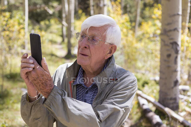 Homem sênior tirando foto com smartphone na trilha da natureza — Fotografia de Stock