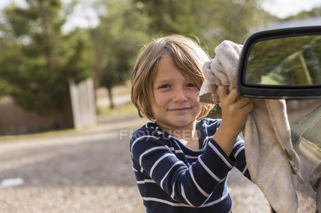 Garçon de quatre ans polissage d'une voiture extérieure avec un nettoyant et un chiffon — Photo de stock