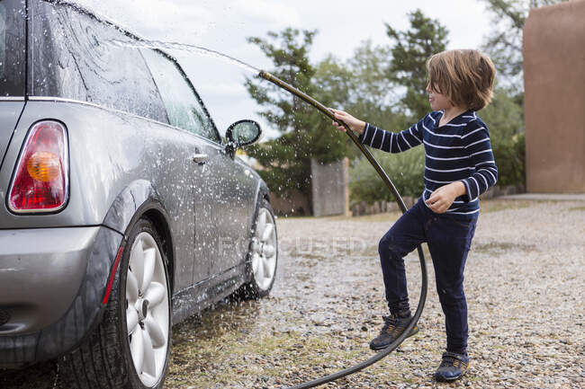 Four year old boy washing a car using a hose — Stock Photo