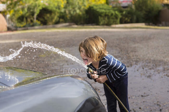 Four year old boy washing a car using a hose — Stock Photo