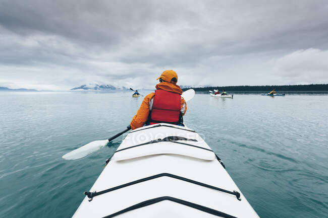 Una persona remando en un kayak de mar doble en aguas tranquilas frente a la costa de Alaska. - foto de stock