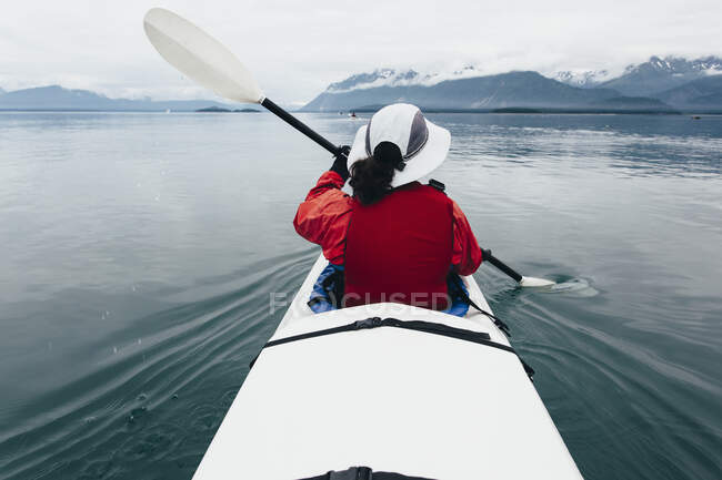 A middle-aged woman paddling sea kayak in the pristine water of Muir Inlet, Glacier Bay National Park and Preserve, Alaska — Stock Photo