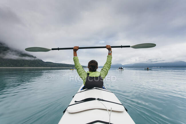 Sea kayaker extends paddle over her head, pristine waters of Muir Inlet in distance, Glacier Bay National Park, Alaska — Stock Photo