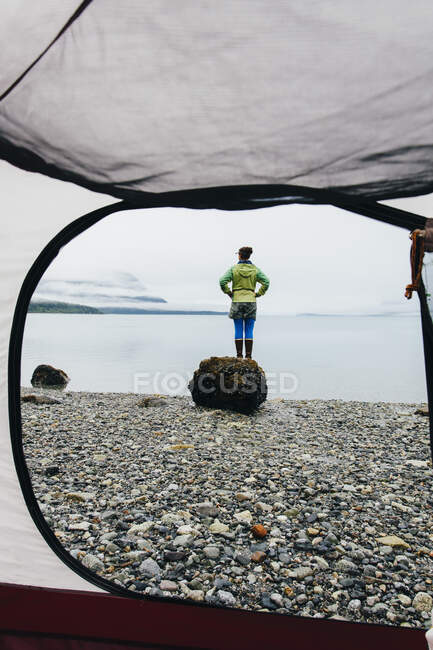 View through camping tent doorway of woman standing on beach,an inlet on the Alaska coastline. — Stock Photo