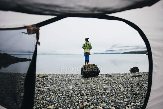 View through camping tent doorway of woman standing on beach,an inlet on the Alaska coastline. — Stock Photo