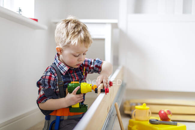 Joven niño usando juguete herramienta eléctrica en casa - foto de stock