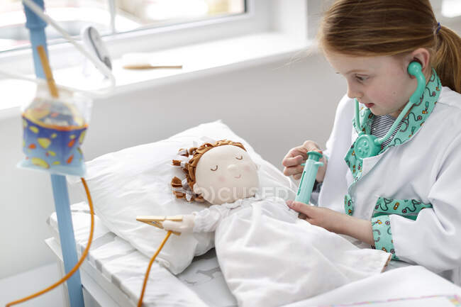 Young girl dressed as doctor pretending to treat patient in make-believe hospital bed — Stock Photo