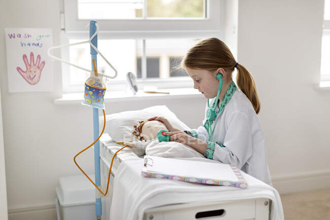 Menina vestida como médico fingindo tratar paciente em make-bleieve cama de hospital — Fotografia de Stock