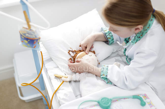 Jeune fille habillée en médecin mettant du plâtre sur la tête de poupée dans un lit d'hôpital imaginaire — Photo de stock