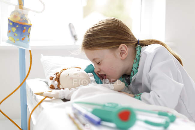 Chica joven vestida como médico fingiendo tratar a paciente en cama de hospital make-bleieve - foto de stock