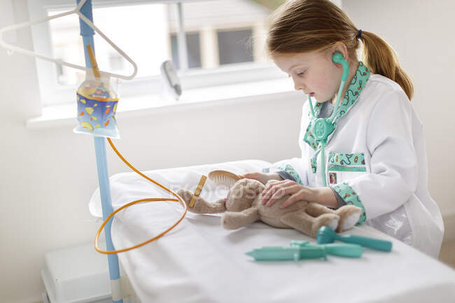 Chica joven vestida como médico fingiendo tratar a los animales de peluche en la cama de hospital make-bleieve - foto de stock