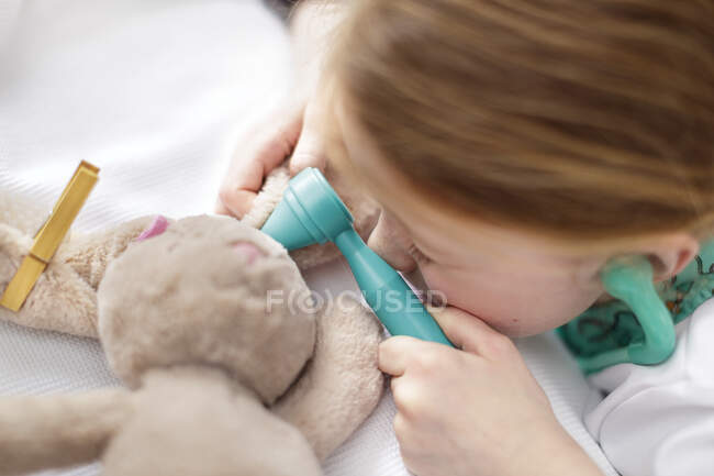 Young girl dressed as doctor pretending to treat toy animal in make-believe hospital bed — Stock Photo
