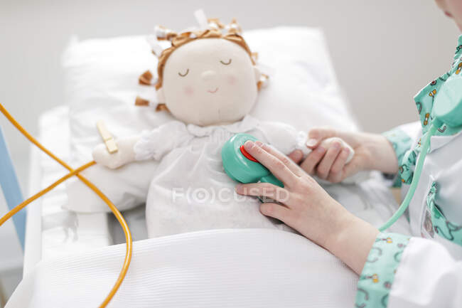 Menina vestida como médico usando estetoscópio de brinquedo na boneca na cama do hospital make-believe — Fotografia de Stock