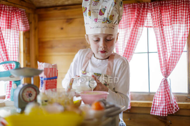 Jovencita en casa de Wendy vertiendo leche fingiendo cocinar en la cocina - foto de stock