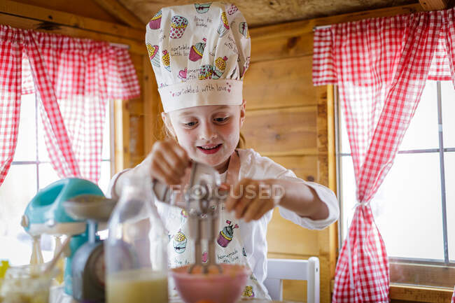 Jeune fille dans wendy maison à l'aide de fouet en plastique prétendant cuisiner dans la cuisine — Photo de stock