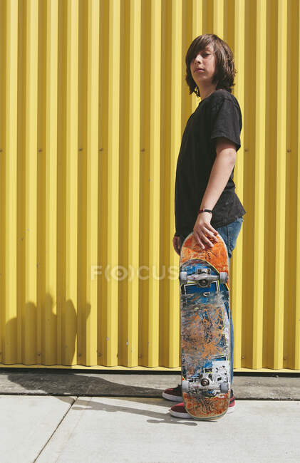 Teenage boy posing with skateboard in front of urban warehouse — Stock Photo