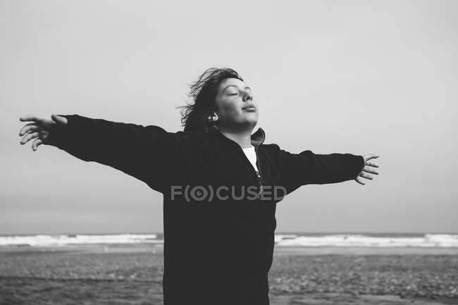 Adolescente na praia com os braços estendidos em direção à brisa, oceano à distância — Fotografia de Stock