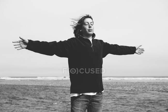 Adolescente en la playa con los brazos extendidos hacia la brisa, océano en la distancia - foto de stock