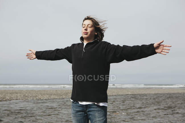 Хлопчик-підліток на пляжі з руками, витягнутими до вітру, океан на відстані — стокове фото