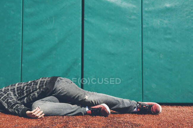 Teenage boy lying down on an athletic field by a blue wall — Stock Photo