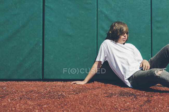 Adolescent garçon assis contre rembourré mur à terrain de sport. — Photo de stock