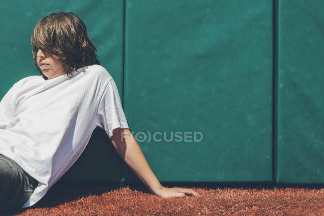 Мальчик-подросток, сидящий у стены на спортивном поле. — стоковое фото