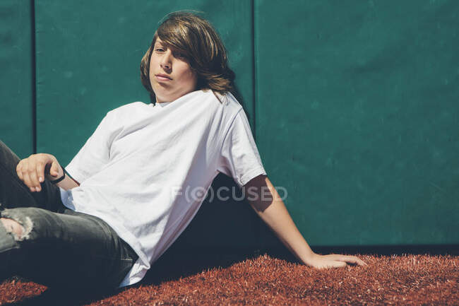 Teenage boy sitting against padded wall at sports field. — Stock Photo