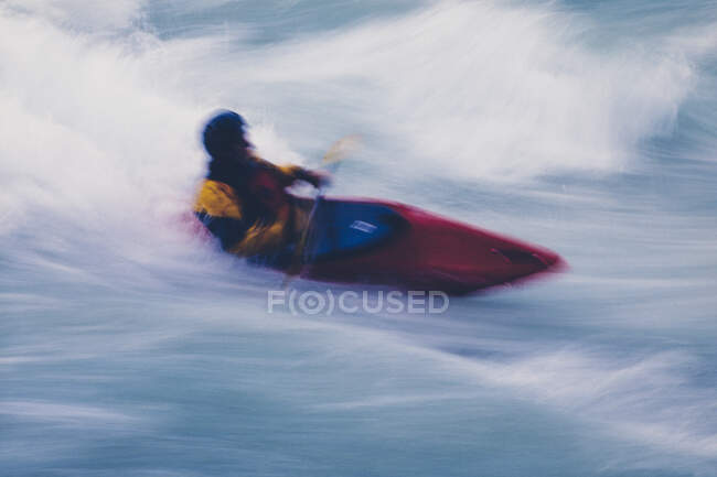 Longue exposition du kayakiste en eau vive mâle pagayant et surfant sur de grands rapides sur une rivière à écoulement rapide. — Photo de stock