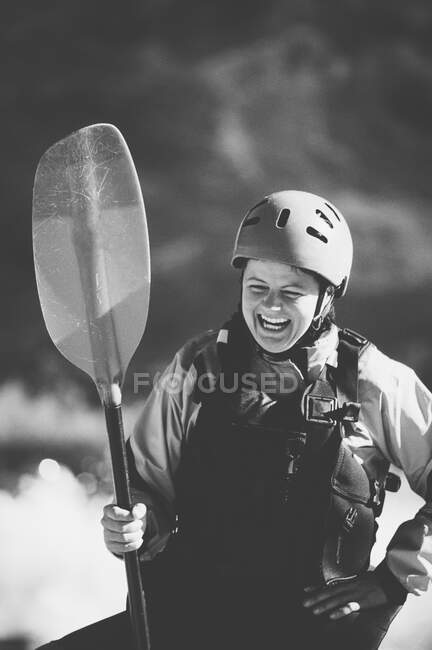 Female whitewater kayaker in helmet and life vest on a river bank holding a paddle. — Stock Photo