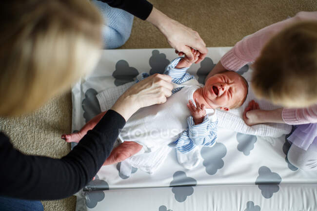 Mother and daugher tending to crying baby on changing mat — Stock Photo