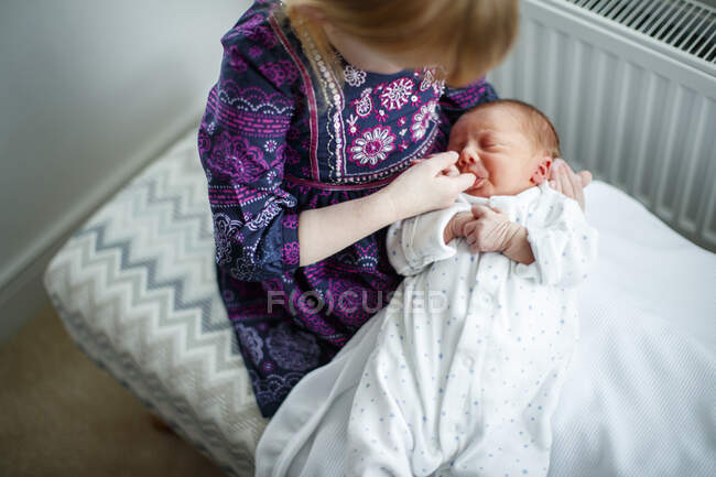 Young girl with finger in mouth of newborn baby on lap — Stock Photo
