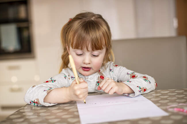Jeune fille écrivant à la table de cuisine — Photo de stock