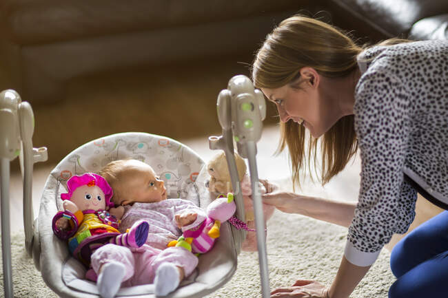 Woman playing with baby surrounded by toys lying in baby swing — Stock Photo