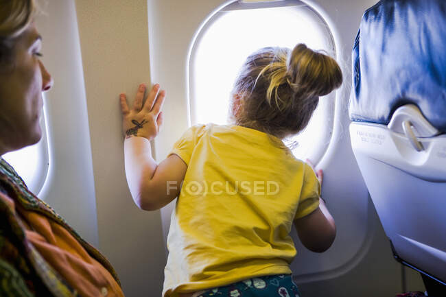 Молодая девушка выглядывает из окна самолета — стоковое фото
